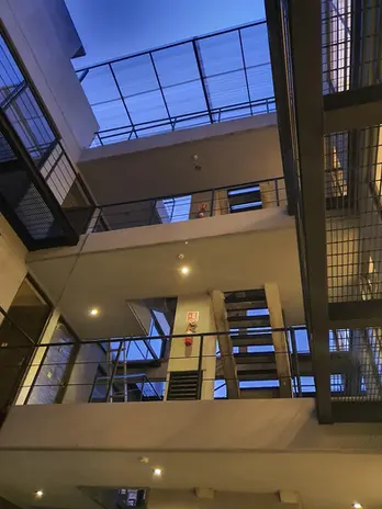 Cubo de luz y pasillos interiores con escaleras modernas, barandales de herrería y un domo transparente que permite iluminación natural.