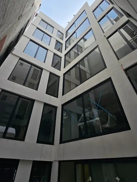 aPerspectiva desde el patio central de un edificio de departamentos, destacando la arquitectura de líneas limpias y ventanales de gran formato que aseguran iluminación natural.