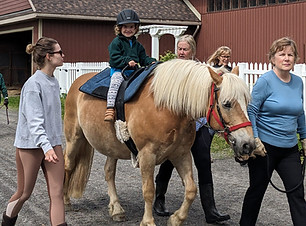 Young child riding pony, guided by instructors.