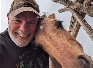 Smiling volunteer with a young horse nuzzling his face