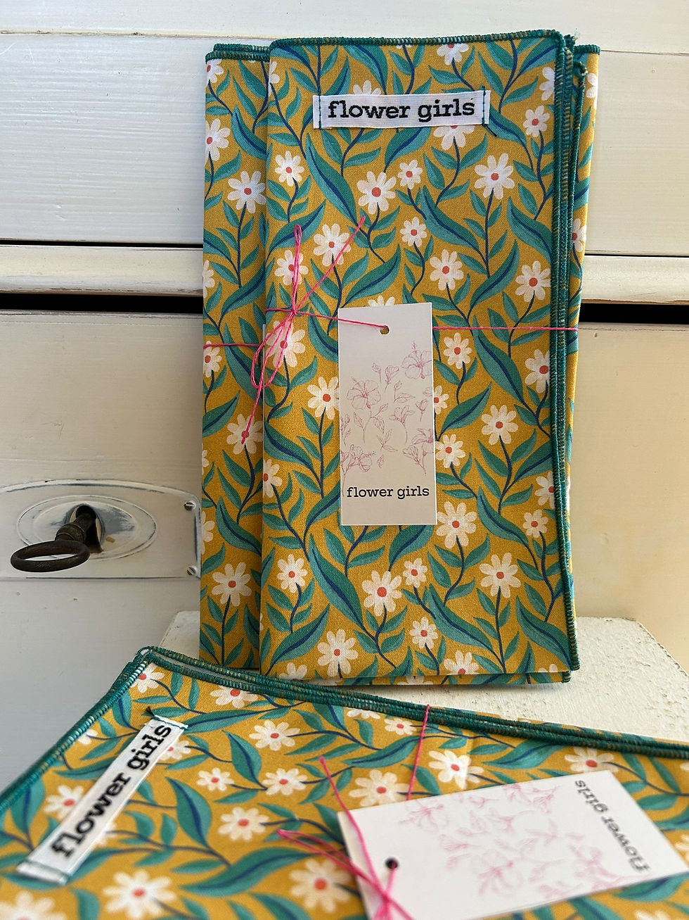 Miniaturbild: Uni weiße Stoffserviette hängt neben einer Blumenmuster Serviette vor einer Holzwand.