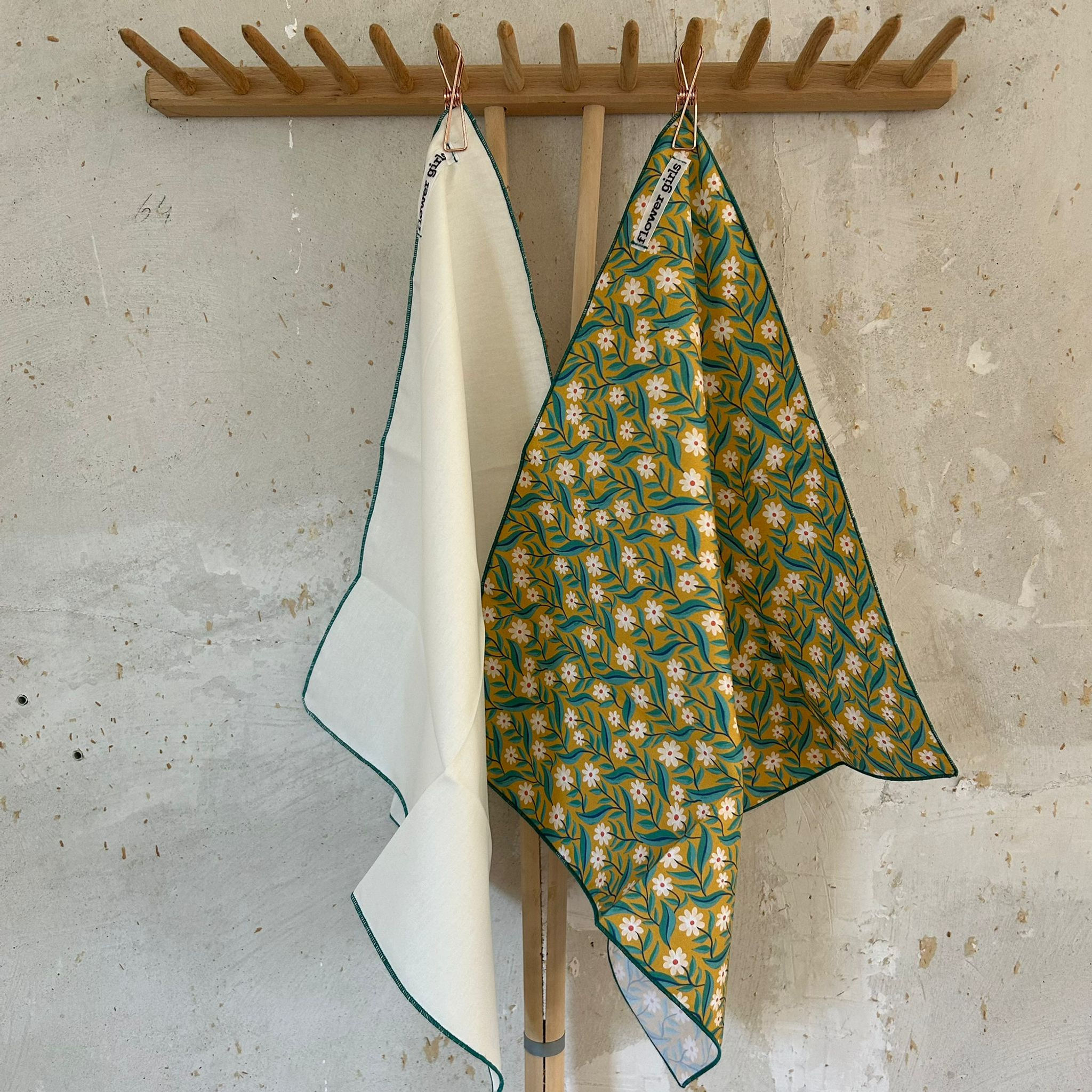 Uni weiße Stoffserviette hängt neben einer Blumenmuster Serviette vor einer Betonwand