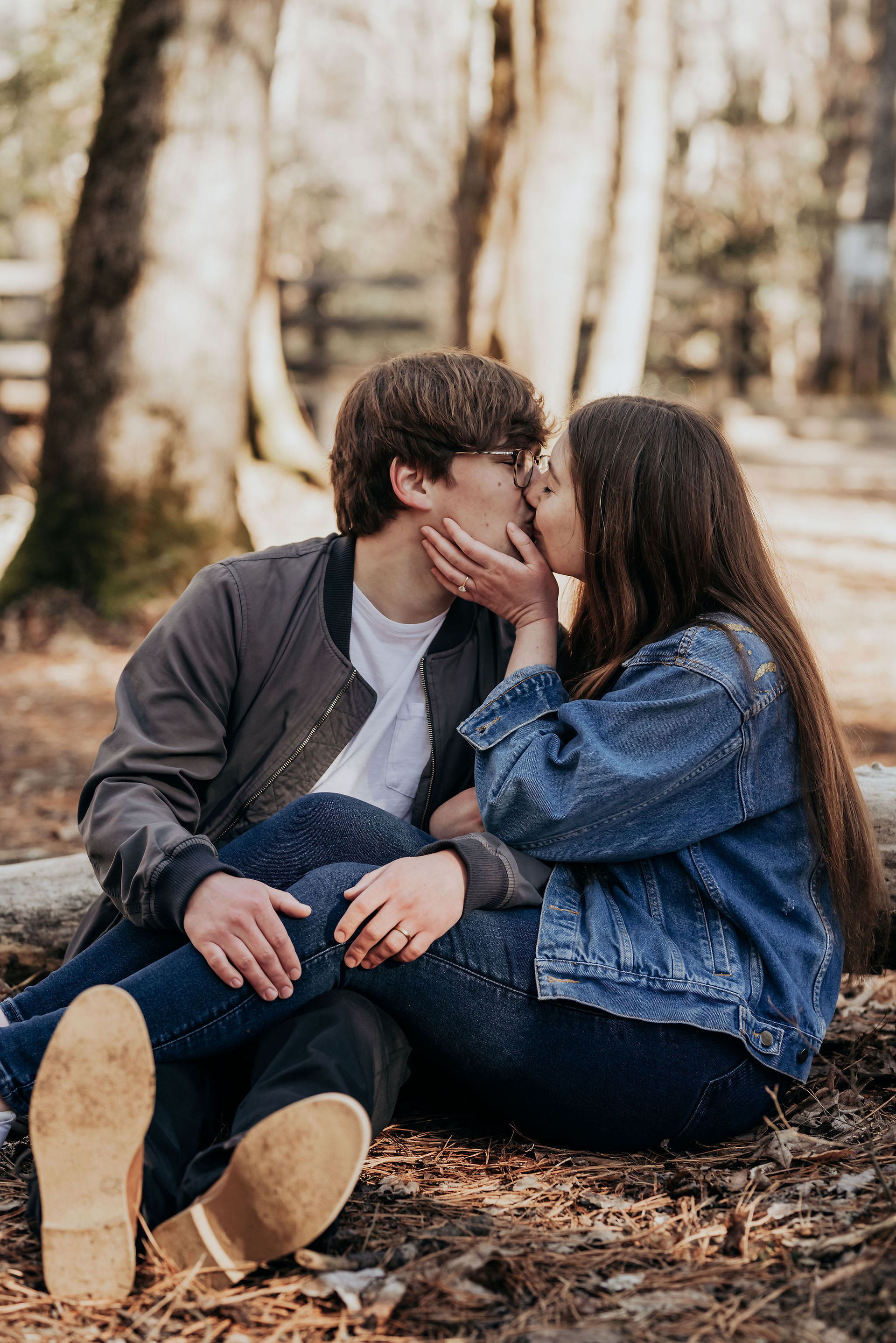 couple sitting on tree kissing in forest at engagement photos at cades cove in tennessee