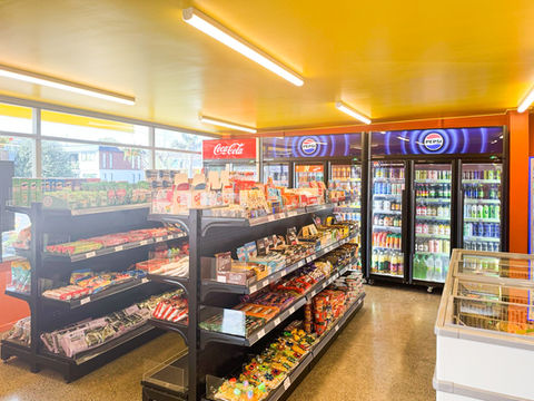 Shelves at Pie2Go showcasing chips, biscuits, noodles, nuts, and snacks, with fridges in the background featuring Pepsi and Coca-Cola drink ranges, and a freezer stocked with frozen foods.