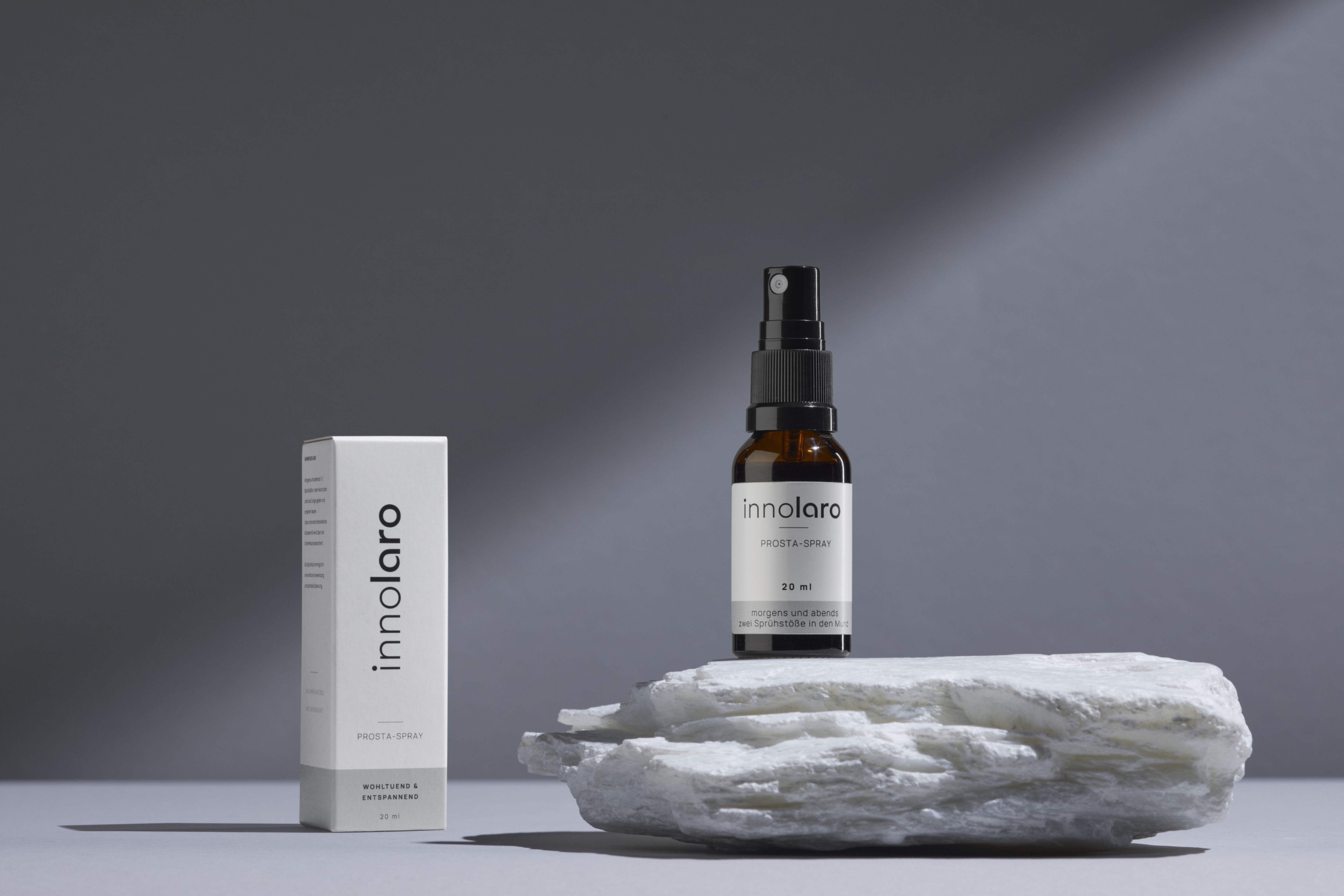 Produkt "Prosta-Spray" Flasche mit Verpackung vor einem grauen Hintergrund, auf einem Naturstein.