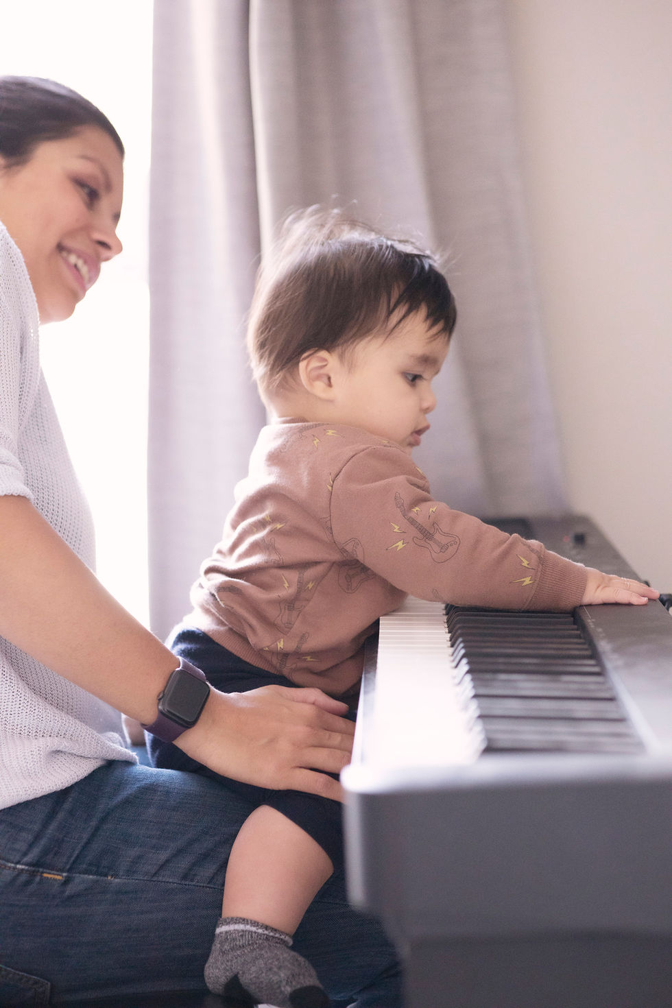 a small child plays the piano while sitting on his mother's lap