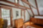The Ilse room has wood beam cathedral ceilings over a wooden queen-sized bed with a dresser and large windows.