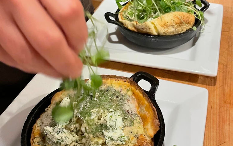 Plating a savory puffed pancake with goat cheese, dill, and watercress topping