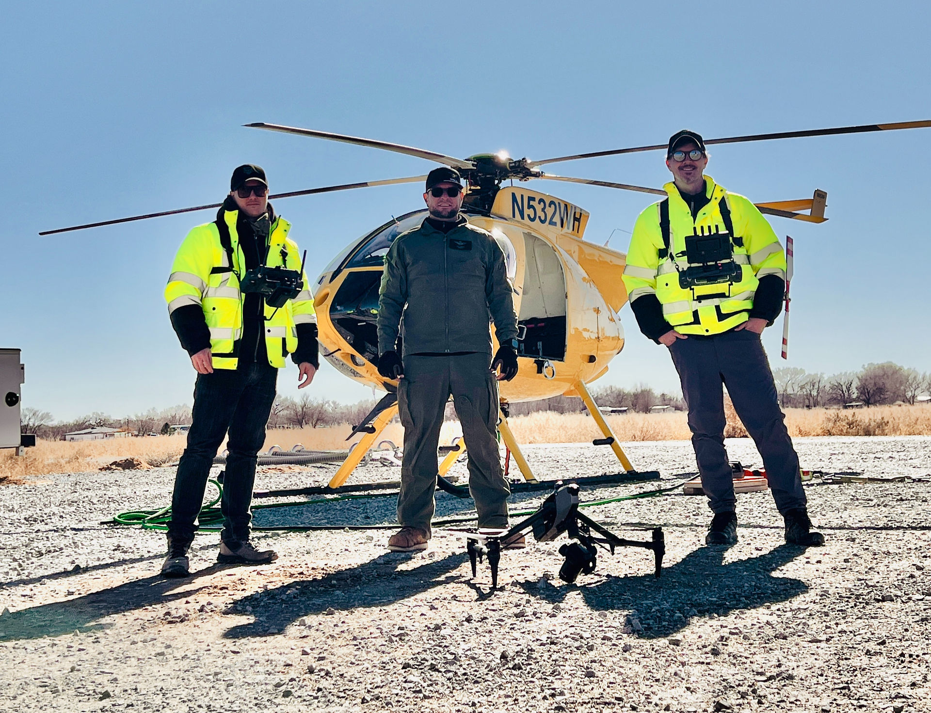 Three men standing in front of a yellow helicopter with a DJI Inspire drone on the ground