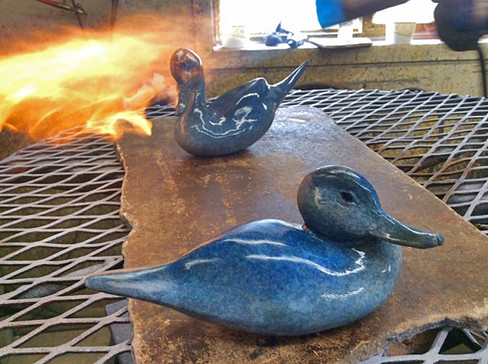 two blue anniversary pintail sculptures by geoffrey smith at the foundry with the one in the back being heated with fire
