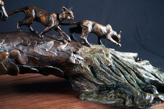 Close up of  bronze sculpture featuring panther cubs walking on top of a fallen palm tree.