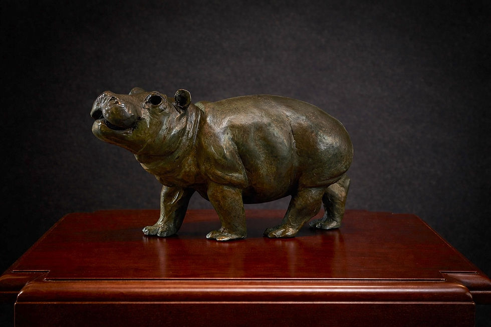 Small bronze hippopotamus sculpture by Geoffrey C. Smith with lifted head and compact stance against a dark background.
