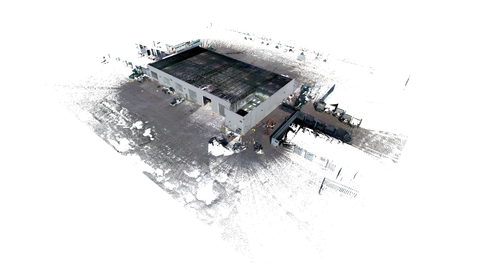 An aerial view of a commercial building with a flat roof, surrounded by a large paved area used for parking. The building features a simple rectangular design with several entrances visible on the front side. Nearby, a variety of vehicles are parked nearby, suggesting activity at the location. The image is rendered with a soft overlay, creating a lightly blurred effect that still allows for clear recognition of the building’s structure and surrounding layout, emphasizing the scale and function of the commercial space.