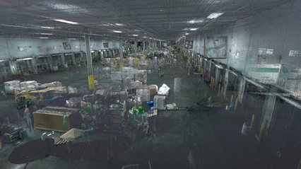 An interior view of a large warehouse space, showcasing a bustling environment filled with various items and equipment scattered throughout. The image captures the expansive layout, with pallets, packages, and machinery visible, indicating active operations. The lighting is bright, illuminating the concrete floors and the high ceilings of the warehouse. The visual presentation has a slight abstract quality, suggesting movement and activity while still showing key details of the working space.