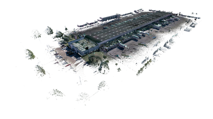  An aerial view of a large commercial building and parking lot, set within a landscaped area. The structure is outlined with multiple sections, showcasing a blend of rooftops and outdoor spaces, including greenery on the roof of the central building. Surrounding the main structure are numerous parked vehicles organized in a spacious parking lot. The image has a soft overlay, creating a dreamlike quality while clearly defining the layout of the buildings and parking configurations, emphasizing the scale of the commercial area.