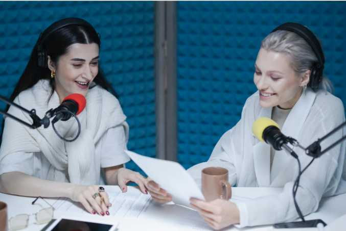 Two women engaged in an energetic podcast recording session, speaking into microphones while sharing technology insights in a modern studio