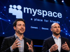 Two speakers stand on stage during a conference presentation, speaking with headset microphones in front of a large screen displaying the MySpace logo.