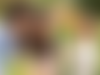 一家年輕幸福的家庭在花園裡。一位深色頭髮、穿著藍色襯衫的男士和一位深色頭髮、穿著米色上衣的女士,正微笑著看著一個小孩。這個小孩有淺棕色頭髮,穿著淺色上衣,手裡拿著一棟微型木屋,正專注地看著它。模糊的背景中有五顏六色的花朵。整張圖片散發著溫馨和歡樂的氣氛。