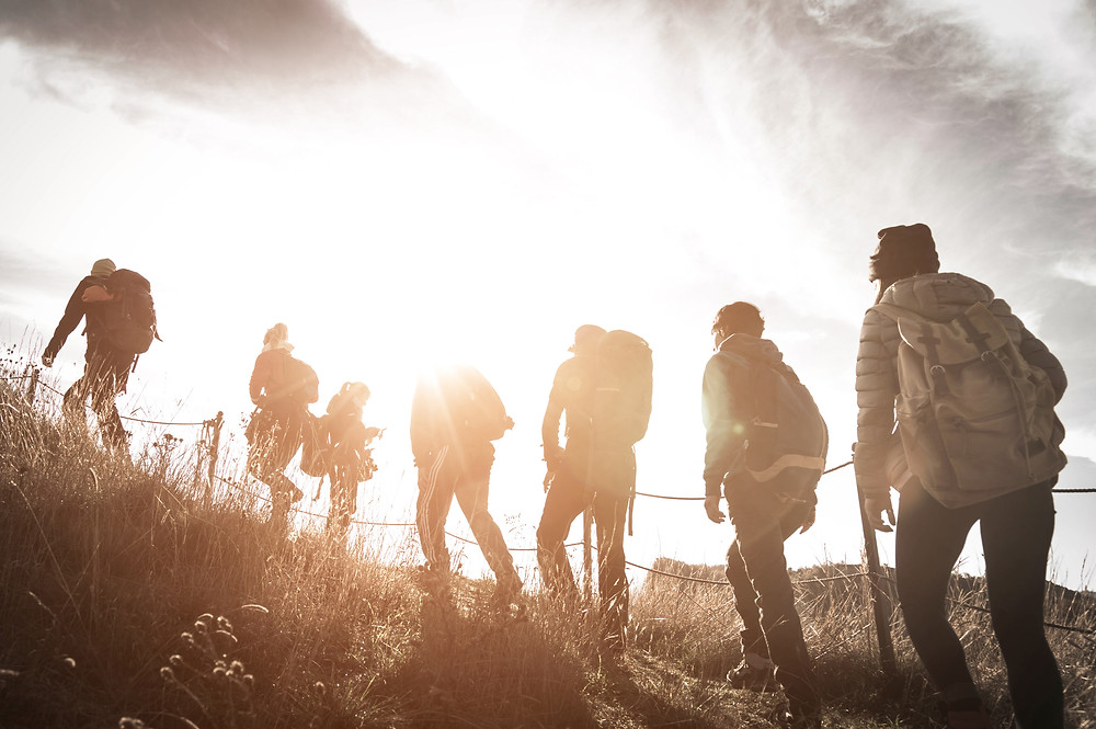 Der Artikel heißt: Backpacking statt all-inclusive – die Reise auf die New-Work-Insel. Das Bild zeigt siebenjunge Personen, die im Sonnenuntergang auf einem Berg Backpacken.