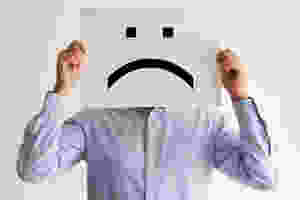 Der Artikel heißt: Der Teufelskreis des kleinen Wehwehchens. Das Bild zeigt einen Mann, der vor sein Gesicht ein Blatt mit aufgemalten Traurig-Smiley hält