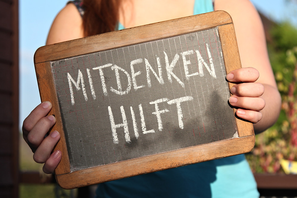 Der Artikel heißt: Führungslos, aber nicht kopflos. Das Bild zeigt: Eine Frau mit einem Schild, dieses trägt die Aufschrift „mitdenken hilft“.