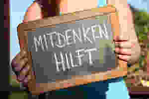 Der Artikel heißt: Führungslos, aber nicht kopflos. Das Bild zeigt: Eine Frau mit einem Schild, dieses trägt die Aufschrift „mitdenken hilft“.