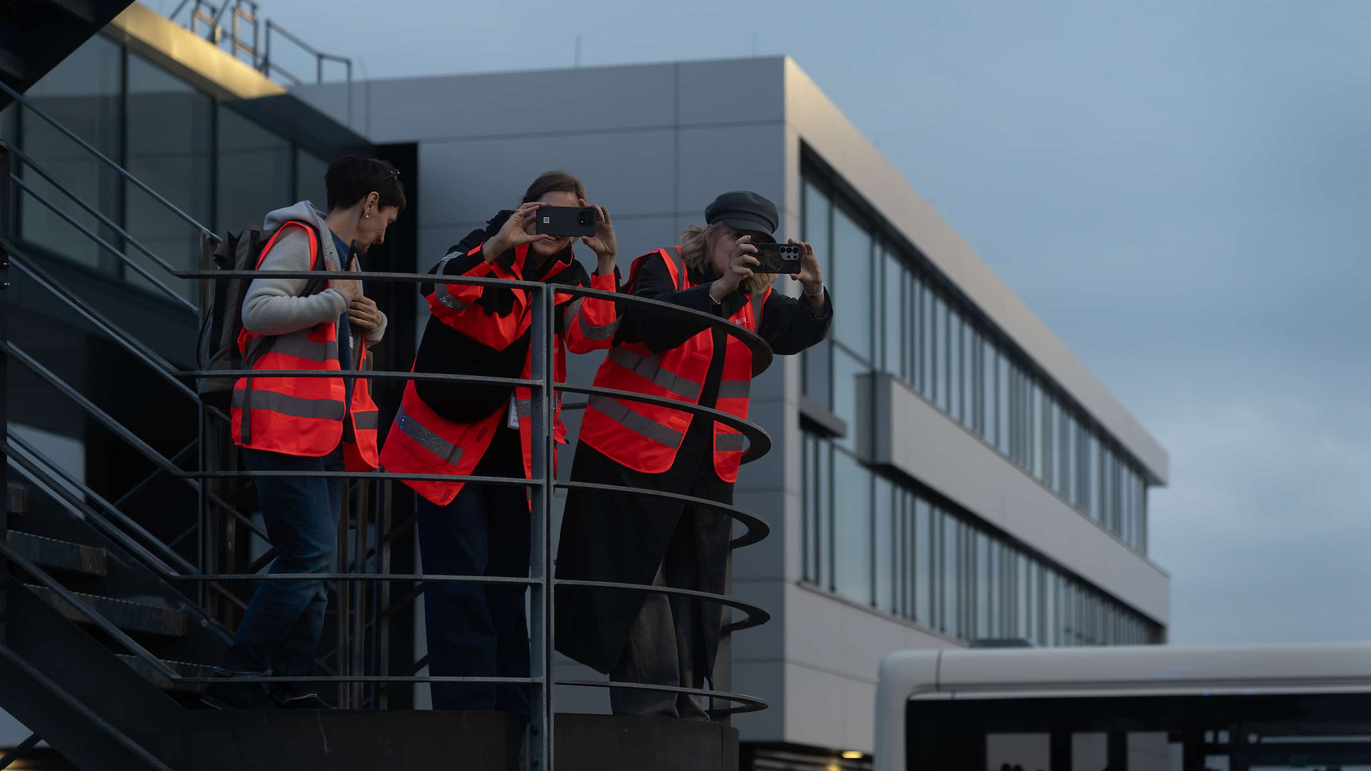 People in safety vests taking photos with smartphones from the observation deck at Berlin Brandenburg Airport.