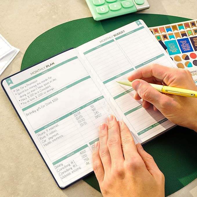 Hands writing in a budget planner with a yellow pen. The planner shows "Monthly Plan" and "Monthly Budget." Green calculator and stickers nearby.