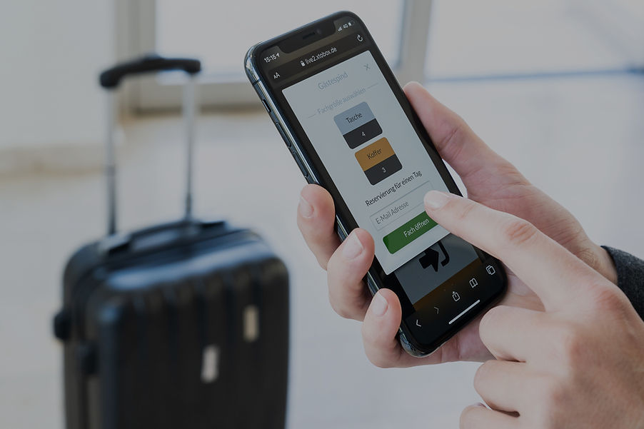 Pareva Smartlocker Software ausgeführt auf einem Smartphone Webbrowser in der Hand einer Frau die mit einem Koffer vor einer Besucher Spind Smartlocker steht