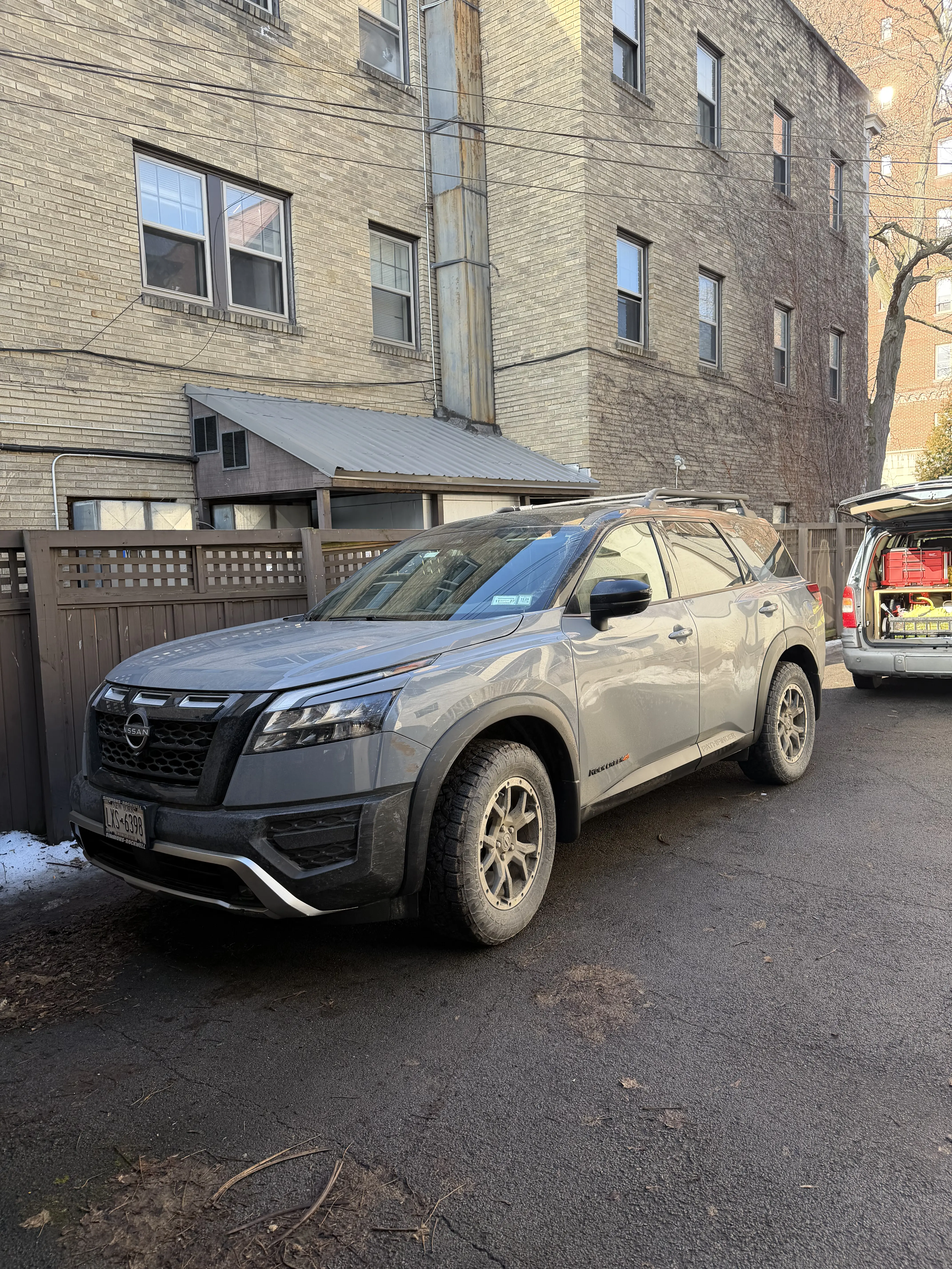 Gray Nissan Pathfinder SUV covered in heavy white winter road salt parked outside a Rochester NY apartment building before professional mobile detailing.