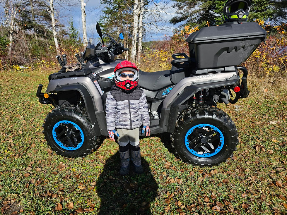 a little boy with his helmet on standing in front of an atv.