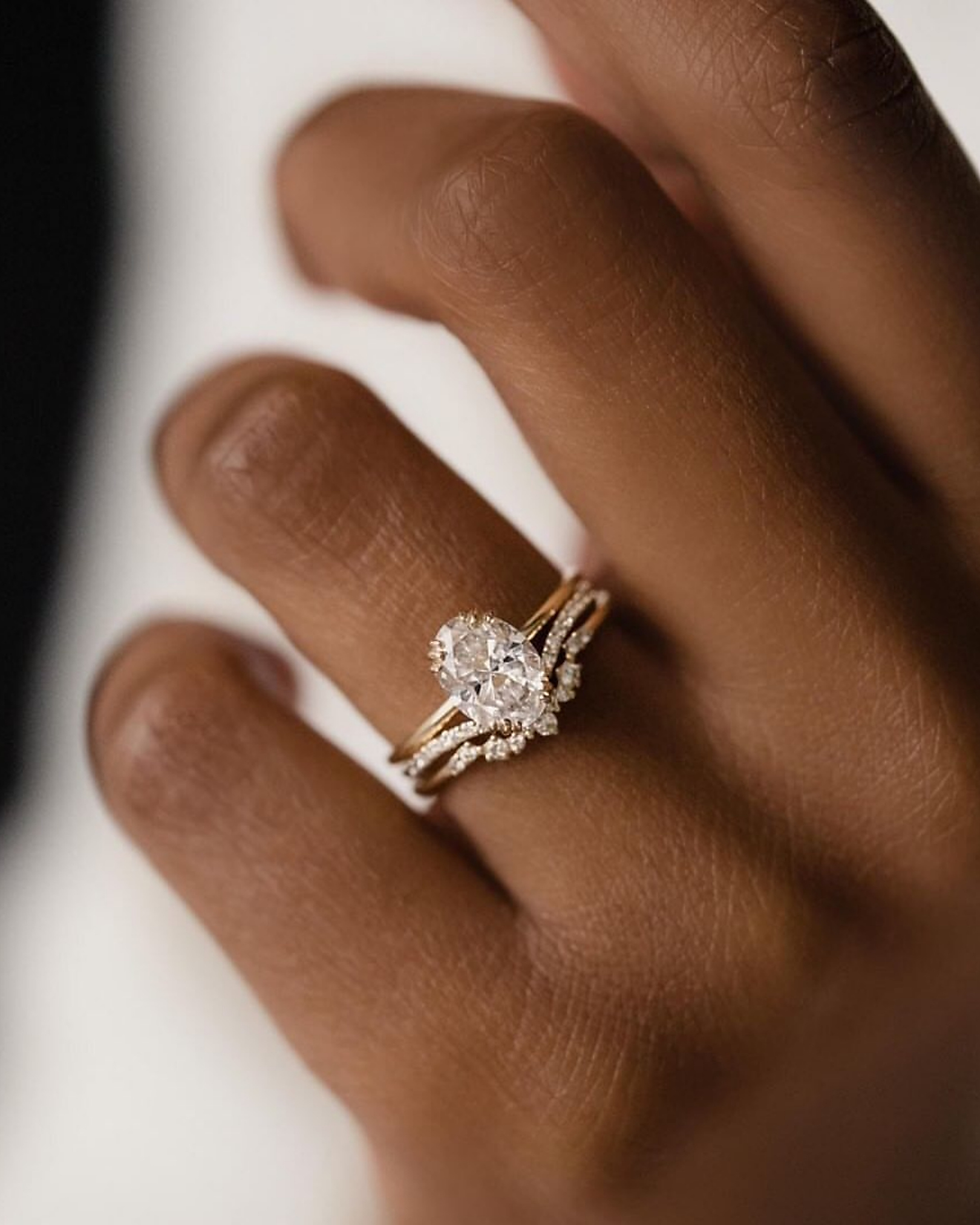 Close-up of a hand wearing a sparkling diamond ring with a gold band and tiny stones on a plain white background