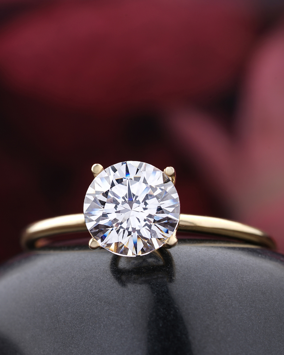 Close-up of a diamond solitaire ring on a black surface, with a blurred burgundy background.