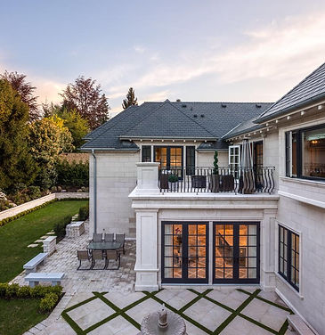 Rear exterior view of luxury residence with landscaped backyard, stone pathways, and large window openings.