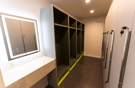 Locker room vanity and storage area with LED-lit mirror, solid-surface countertop, and custom millwork lockers.