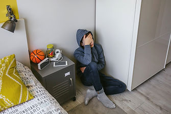 Unrecognizable depressed male teenager with his hand on his head sitting on the floor in h