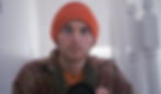 A monk wearing an orange hat takes a selfie with a camera