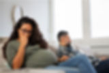 Anxious pregnant mother sitting on sofa with man in plaid shirt.