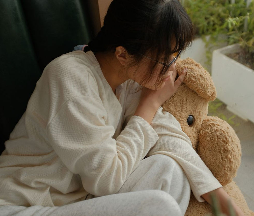 A young woman in casual wear relaxing with a teddy bear by a window.