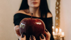 Blurred woman presenting a vivid red apple in focus, adding mystery.