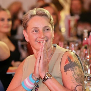 Kate at a dinner clasping hands together wearing a transgender flag armband