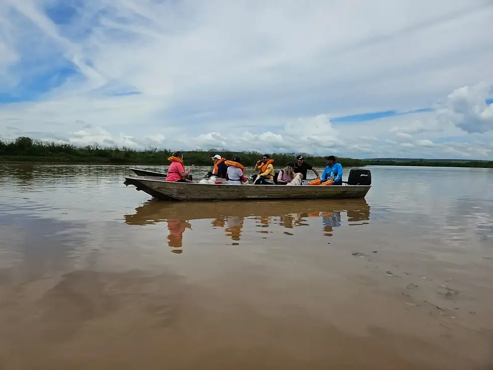 Um grupo de pessoas em um barco no rio, rodeados pela natureza, em um dia ensolarado. Os participantes usam coletes salva-vidas e há um clima de aventura na imagem.