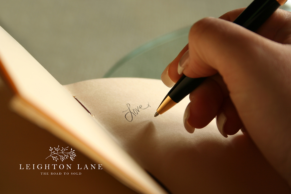 Hand writes love in a notebook with a black pen; Leighton Lane logo and The Road to Sold appear at bottom.