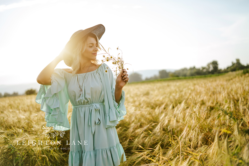 Woman in a mint dress and sunhat holding wildflowers in a sunlit wheat field; Leighton Lane logo at bottom.