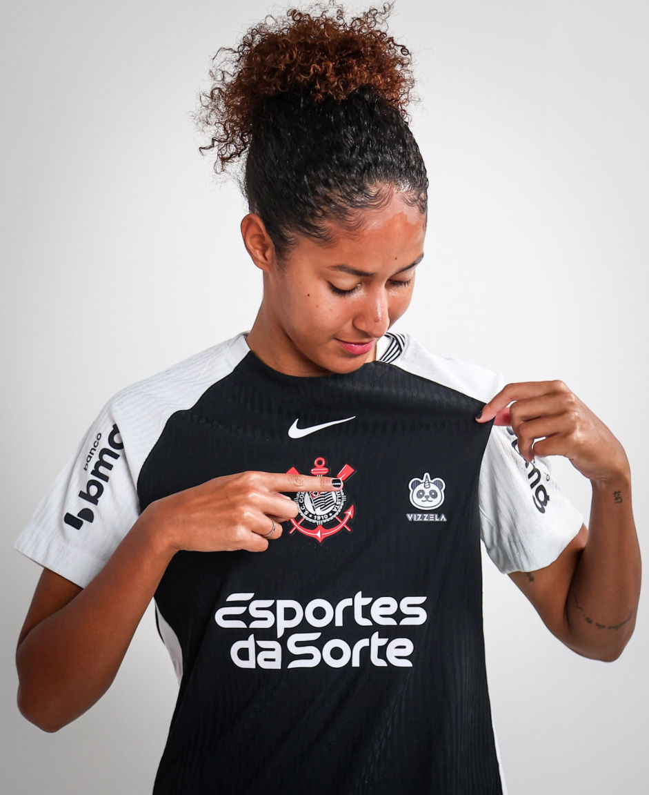 Gi Fernandes do Corinthians aponta para a marca da Vizzela estampada no peito do uniforme das Brabas.
