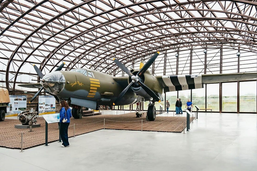 Visitors view a WWII bomber in a modern museum hangar with arched steel roof and striped wings, calm and spacious interior.