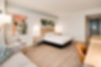Hotel room with a modern design. Features a bed, wooden nightstands, a desk with an orange chair, abstract art, and soft lighting. Relaxing mood.