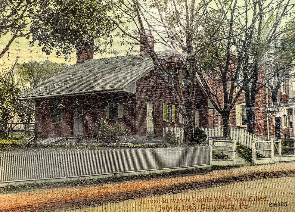 Historic brick house with white fence and trees. Sign reads "Jennie Wade House." Text at bottom notes Gettysburg, July 3, 1863.