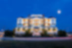 Illuminated Hotel LBI at night, glowing against a deep blue sky with a crescent moon. Bright facade with warm lights and greenery.