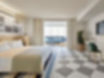 Modern hotel room with a double bed, checkered floor, and a seating area by the window. Neutral tones, wall art, and a potted plant.